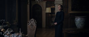 Movie still from “Rebecca” (2020), directed by Ben Wheatley – A woman standing in front of a chair in a room; Medium shot, Low angle