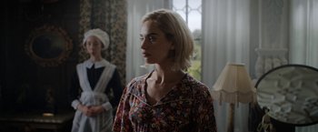 Movie still from “Rebecca” (2020), directed by Ben Wheatley – A woman with blonde hair wearing a floral dress; Medium shot, Over the shoulder angle