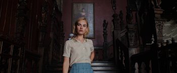 Movie still from “Rebecca” (2020), directed by Ben Wheatley – A woman standing in front of a painting in a room; Medium shot, Low angle