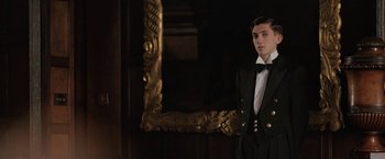 Movie still from “Rebecca” (2020), directed by Ben Wheatley – A man in a suit and tie standing in front of a mirror; Medium shot, Low angle