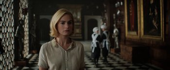 Movie still from “Rebecca” (2020), directed by Ben Wheatley – A woman standing in front of a group of people; Medium shot, Over the shoulder angle