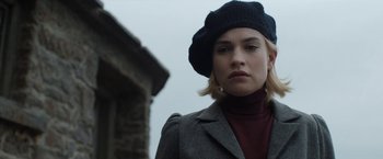Movie still from “Rebecca” (2020), directed by Ben Wheatley – A woman wearing a black hat and a gray jacket; Close Up shot, Low angle