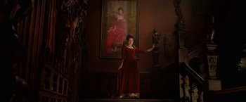 Movie still from “Rebecca” (2020), directed by Ben Wheatley – A woman in a red dress standing in front of a painting; Wide shot, Low angle