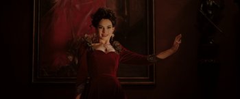 Movie still from “Rebecca” (2020), directed by Ben Wheatley – A woman in a red dress posing in front of a painting; Medium shot, Low angle