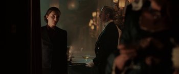 Movie still from “Rebecca” (2020), directed by Ben Wheatley – A man holding a martini glass in front of another man; Medium shot, Over the shoulder angle