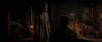 Movie still from “Rebecca” (2020), directed by Ben Wheatley – A woman standing next to a man in a dark room; Medium shot, Over the shoulder angle