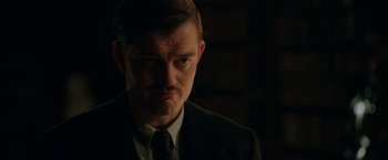 Movie still from “Rebecca” (2020), directed by Ben Wheatley – A man in a suit and tie in a dark room; Close Up shot, Low angle