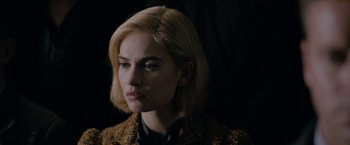 Movie still from “Rebecca” (2020), directed by Ben Wheatley – A woman with blonde hair wearing a brown jacket; Close Up shot, Over the shoulder angle