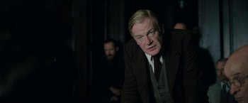 Movie still from “Rebecca” (2020), directed by Ben Wheatley – An older man wearing a suit and tie; Medium shot, Over the shoulder angle