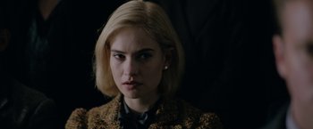 Movie still from “Rebecca” (2020), directed by Ben Wheatley – A woman with blonde hair wearing a jacket and a bow tie; Close Up shot, Over the shoulder angle