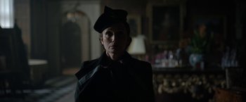 Movie still from “Rebecca” (2020), directed by Ben Wheatley – A woman wearing a hat in a dark room; Medium shot, Low angle