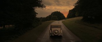 Movie still from “Rebecca” (2020), directed by Ben Wheatley – An old car driving down the road at sunset; Extreme Wide shot, High angle
