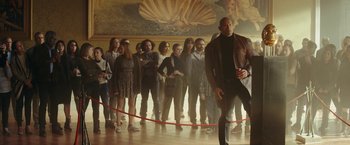 Movie still from “Red Notice” (2021), directed by Rawson Marshall Thurber – A group of people standing in front of a painting; Wide shot, Low angle