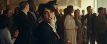 Movie still from “Red Notice” (2021), directed by Rawson Marshall Thurber – A woman standing in a crowd wearing a suit; Close Up shot, Over the shoulder angle