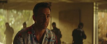 Movie still from “Red Notice” (2021), directed by Rawson Marshall Thurber – A man in a colorful shirt is looking at the camera; Close Up shot, Over the shoulder angle