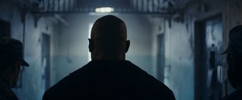 Movie still from “Red Notice” (2021), directed by Rawson Marshall Thurber – A man with a bald head in a dark room; Medium shot, Low angle