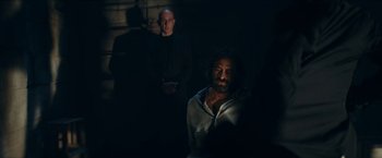 Movie still from “Red Notice” (2021), directed by Rawson Marshall Thurber – A man standing next to another man in a dark room; Medium shot, Over the shoulder angle