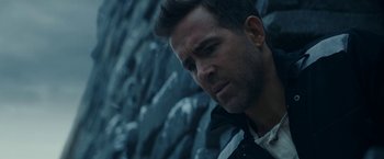 Movie still from “Red Notice” (2021), directed by Rawson Marshall Thurber – A person wearing a jacket near a rock wall; Close Up shot, Over the shoulder angle