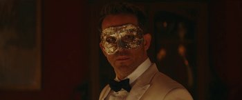 Movie still from “Red Notice” (2021), directed by Rawson Marshall Thurber – A man in a suit wearing a mask and a bow tie; Close Up shot, Over the shoulder angle