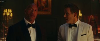 Movie still from “Red Notice” (2021), directed by Rawson Marshall Thurber – Two men in tuxedos standing next to each other; Medium shot, Over the shoulder angle