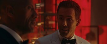Movie still from “Red Notice” (2021), directed by Rawson Marshall Thurber – A person wearing a suit and a bow tie; Close Up shot, Over the shoulder angle