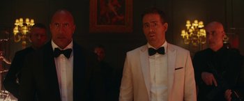 Movie still from “Red Notice” (2021), directed by Rawson Marshall Thurber – Two men in tuxedos standing in a darkened room; Medium shot, Low angle