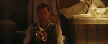 Movie still from “Red Notice” (2021), directed by Rawson Marshall Thurber – A man wearing a vest and holding a boxing belt; Close Up shot, Over the shoulder angle