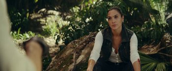 Movie still from “Red Notice” (2021), directed by Rawson Marshall Thurber – A woman sitting on the ground near a tree; Medium shot, Over the shoulder angle