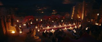 Movie still from “Red Notice” (2021), directed by Rawson Marshall Thurber – A crowd of people sitting on a beach at night; Extreme Wide shot, High angle