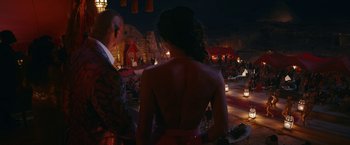 Movie still from “Red Notice” (2021), directed by Rawson Marshall Thurber – A man and a woman standing next to each other in front of a stage; Medium shot, Over the shoulder angle