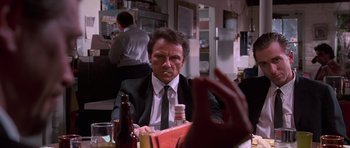 Movie still from “Reservoir Dogs” (1992), directed by Quentin Tarantino – A man sitting at a table in front of a bottle of beer; Medium shot, Over the shoulder angle