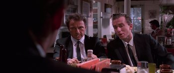 Movie still from “Reservoir Dogs” (1992), directed by Quentin Tarantino – Two men in suits sitting at a table with drinks; Medium shot, Low angle