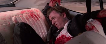 Movie still from “Reservoir Dogs” (1992), directed by Quentin Tarantino – A man in a suit and tie laying in the back of a car; Medium shot, High angle
