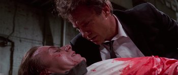 Movie still from “Reservoir Dogs” (1992), directed by Quentin Tarantino – A man in a black suit and a white shirt is holding a knife over a man's face; Close Up shot, Low angle
