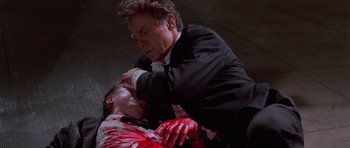 Movie still from “Reservoir Dogs” (1992), directed by Quentin Tarantino – A man in a black suit and white shirt and a man in a black suit and white shirt with blood all over his face and neck; Medium shot, High angle
