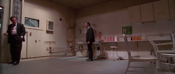 Movie still from “Reservoir Dogs” (1992), directed by Quentin Tarantino – A man standing in front of a table in a room; Wide shot, Low angle