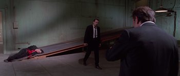 Movie still from “Reservoir Dogs” (1992), directed by Quentin Tarantino – A man wearing a suit and tie walking in a building; Wide shot, Over the shoulder angle