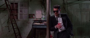 Movie still from “Reservoir Dogs” (1992), directed by Quentin Tarantino – A man in a suit and sunglasses holding a drink; Wide shot, Low angle