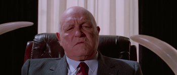 Movie still from “Reservoir Dogs” (1992), directed by Quentin Tarantino – An older man wearing a suit and red tie sitting in an office chair; Close Up shot, Low angle