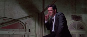 Movie still from “Reservoir Dogs” (1992), directed by Quentin Tarantino – A man in a suit and tie sitting down; Medium shot, Low angle