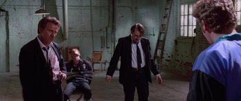 Movie still from “Reservoir Dogs” (1992), directed by Quentin Tarantino – A man in a black suit and a man in a white shirt and black tie; Wide shot, High angle