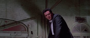 Movie still from “Reservoir Dogs” (1992), directed by Quentin Tarantino – A man wearing a suit and tie standing in a room; Medium shot, Low angle