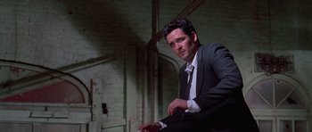 Movie still from “Reservoir Dogs” (1992), directed by Quentin Tarantino – A man in a suit and tie sitting in a room; Medium shot, Low angle