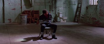 Movie still from “Reservoir Dogs” (1992), directed by Quentin Tarantino – A man sitting on a chair in a dark room; Wide shot, High angle