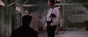 Movie still from “Reservoir Dogs” (1992), directed by Quentin Tarantino – A man in a white shirt and black pants standing next to another man in a white shirt; Medium shot, Low angle