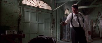 Movie still from “Reservoir Dogs” (1992), directed by Quentin Tarantino – A man holding a gun while standing in a room; Medium shot, Low angle