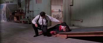 Movie still from “Reservoir Dogs” (1992), directed by Quentin Tarantino – Two men dressed in suits and ties , one of which is lying on the ground and the other is holding a knife; Wide shot, High angle