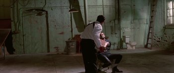 Movie still from “Reservoir Dogs” (1992), directed by Quentin Tarantino – A man standing next to a man sitting on a chair; Wide shot, High angle