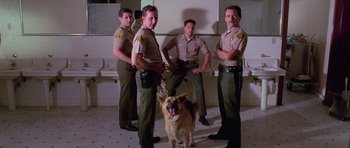Movie still from “Reservoir Dogs” (1992), directed by Quentin Tarantino – A group of men and a dog standing next to each other in front of urinals; Wide shot, Low angle