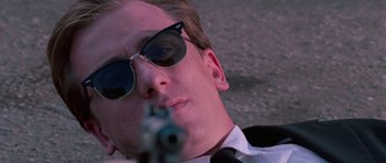 Movie still from “Reservoir Dogs” (1992), directed by Quentin Tarantino – A man in sunglasses and a tie is holding a gun; Close Up shot, Low angle